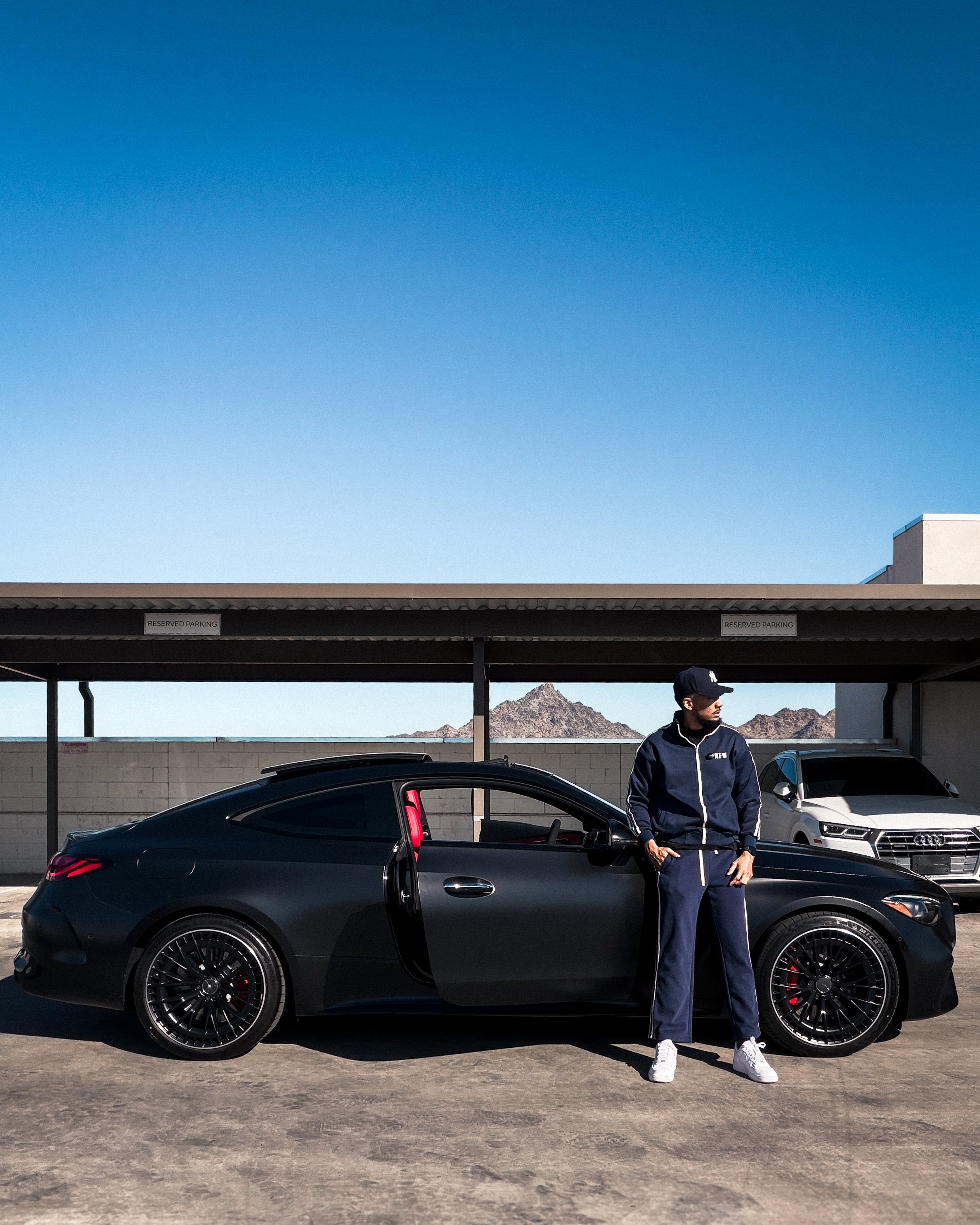 Nate Barnes, founder of FRFW, standing beside his matte-black AMG coupe on a rooftop deck